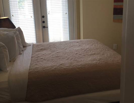 A bed with white sheets and pillows in front of an open door.